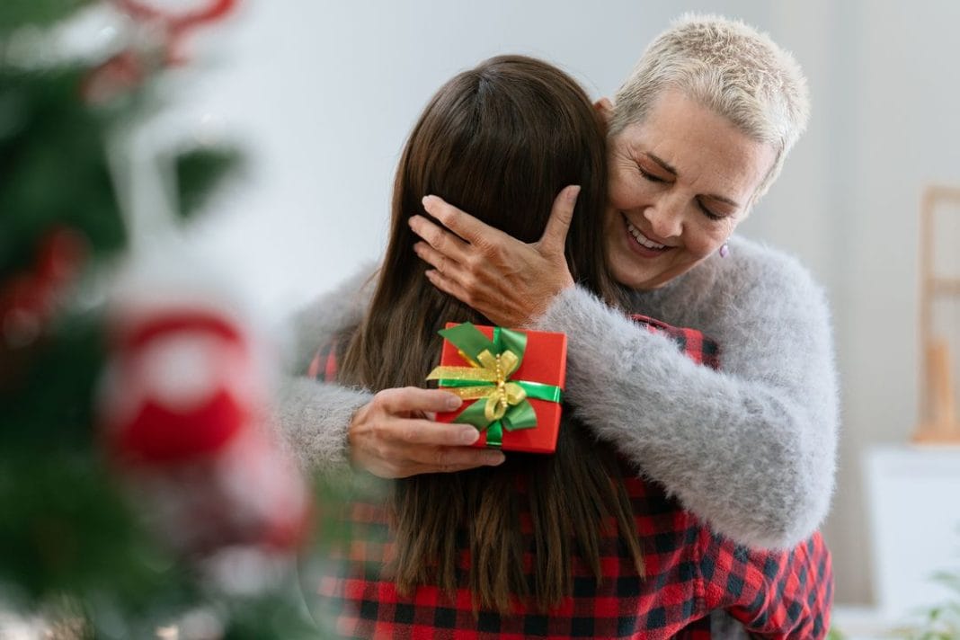 Thankful Caucasian woman with christmas gift hugging daughter at home