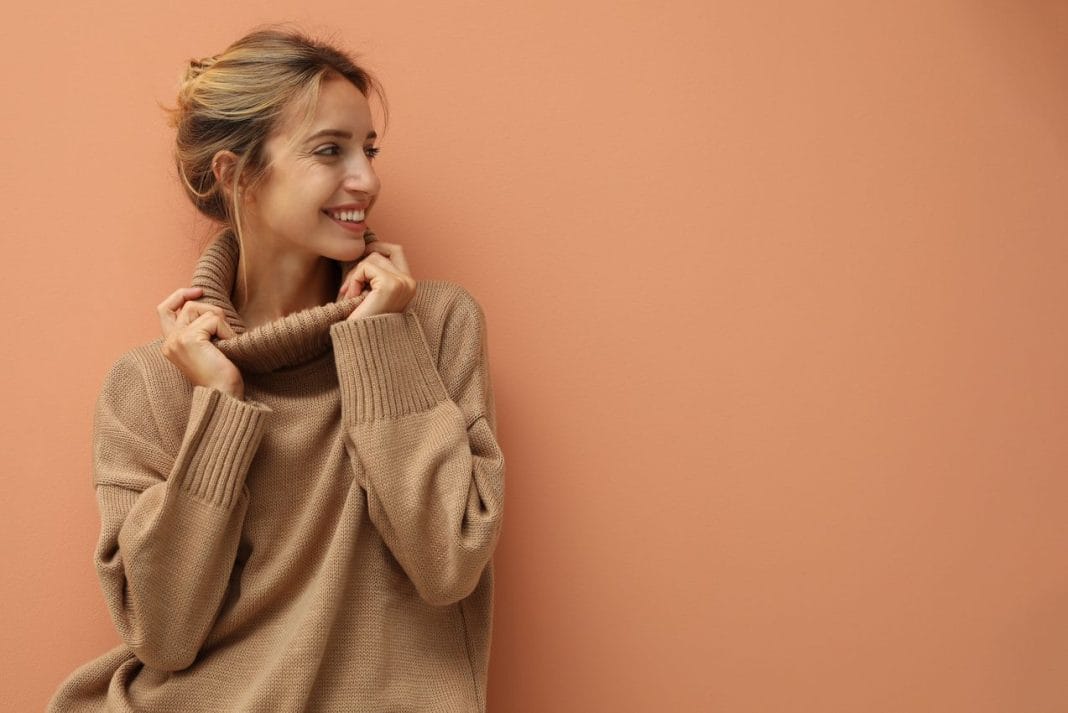 Beautiful young woman wearing knitted sweater on light brown background. Space for text Choix pull de qualité pour femme