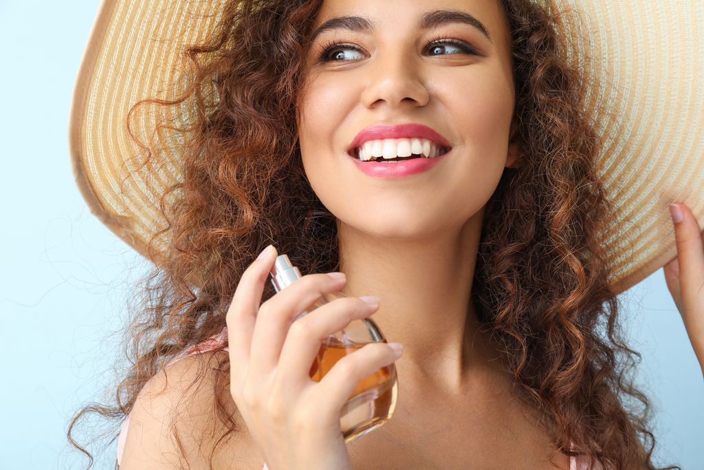 Happy African-American woman with perfume bottle on color background